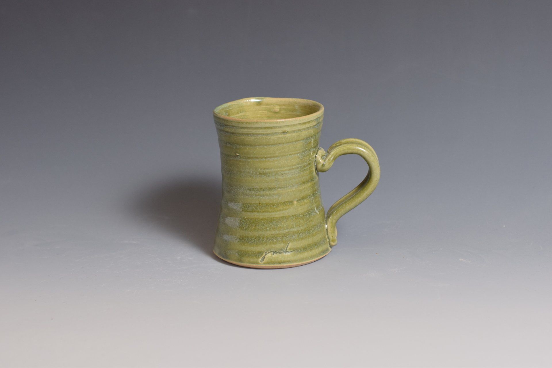 a green mug with a heart shaped handle is sitting on a table .