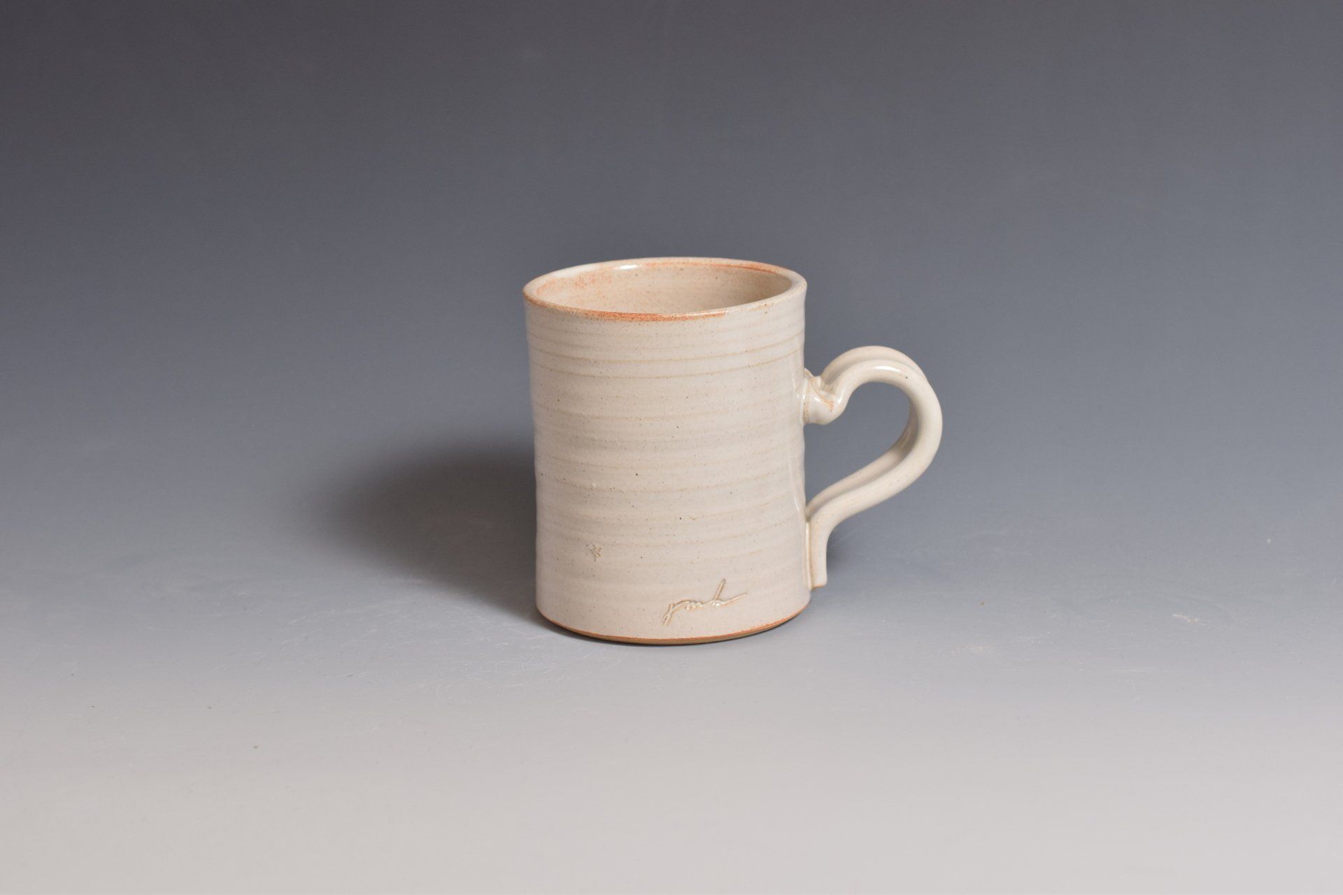 a white mug with a heart shaped handle is sitting on a table .