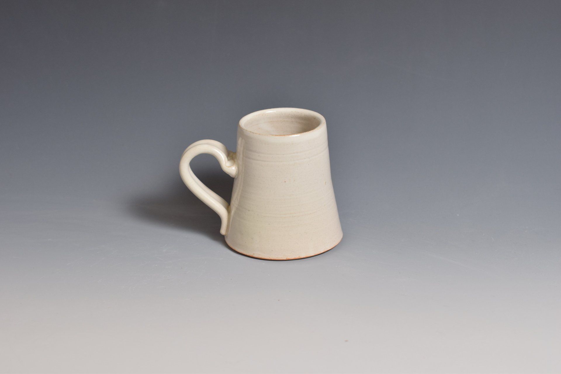 a white mug with a handle is sitting on a gray surface .