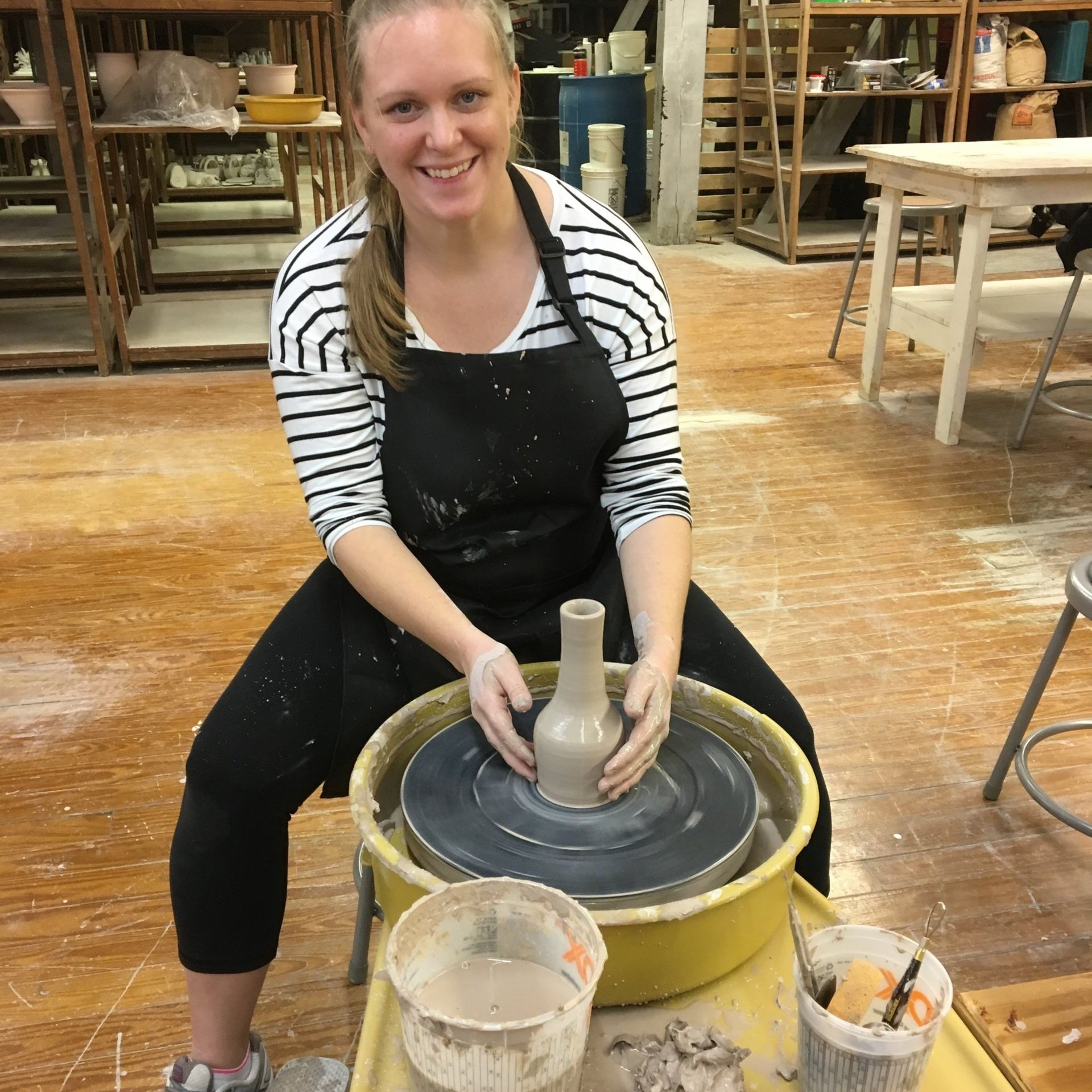 a woman sits on a pottery wheel making a vase