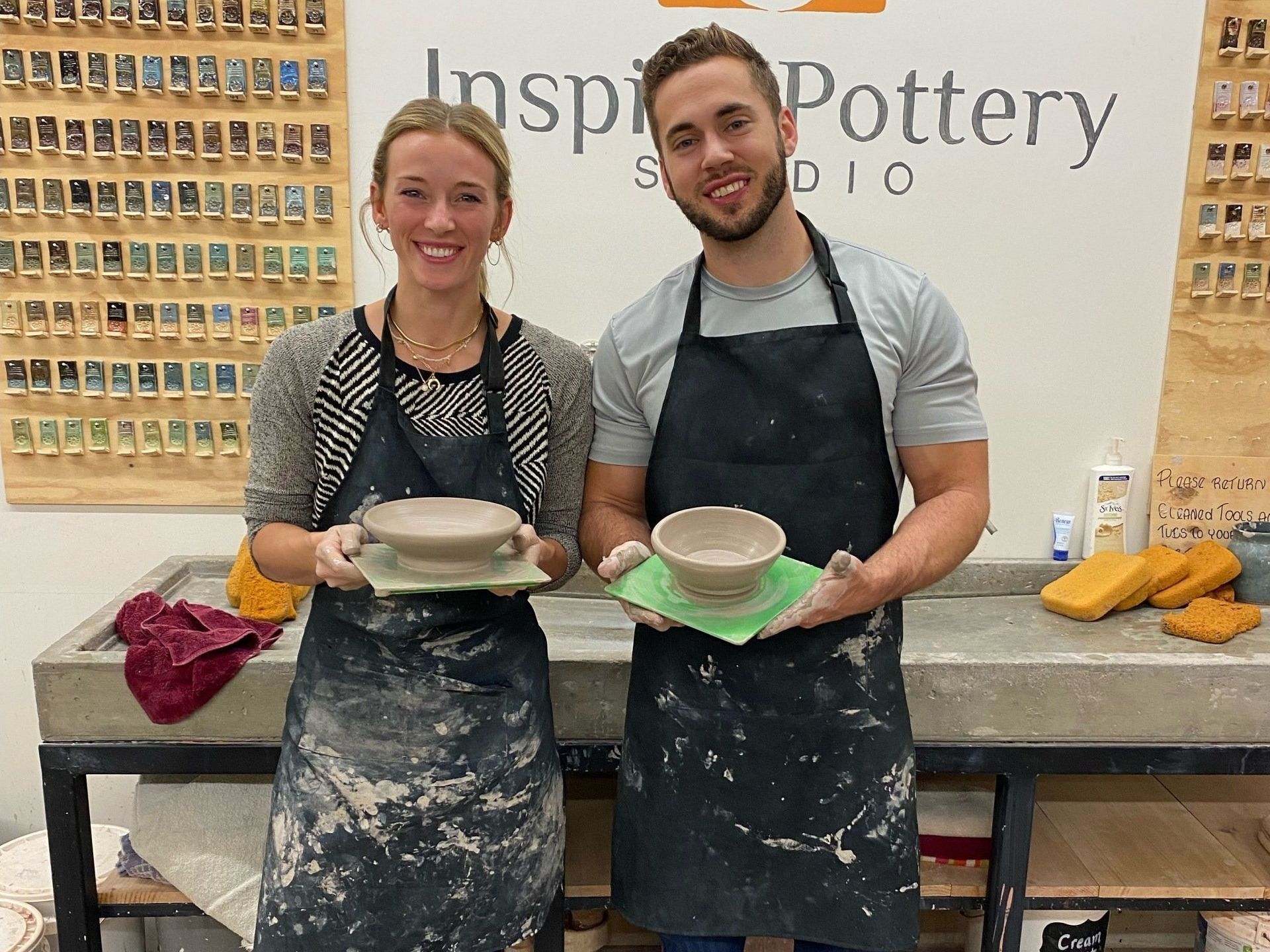 a man and a woman are holding bowls in front of a sign that says inspire pottery studio