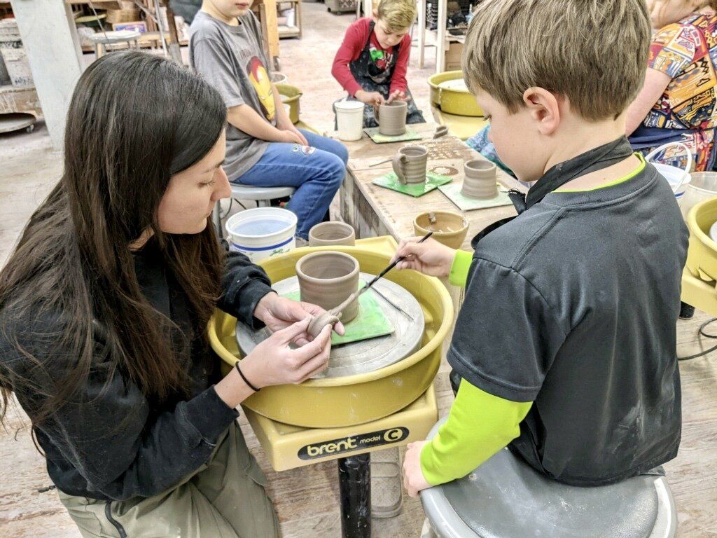 a woman is teaching a boy how to use a pottery wheel .