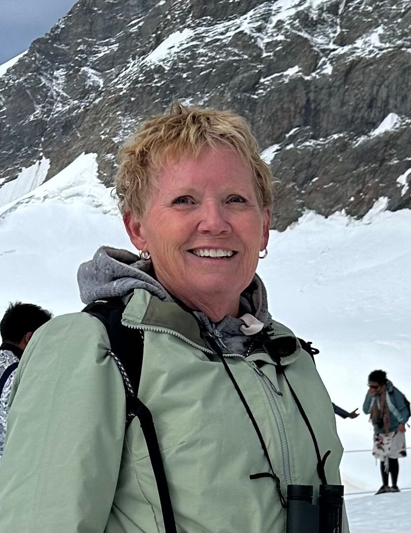 A woman wearing binoculars is standing in front of a snowy mountain.