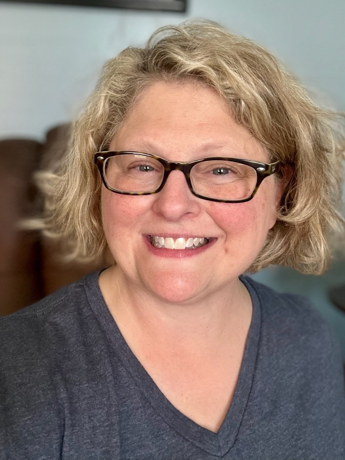 A woman wearing glasses and a gray shirt is smiling for the camera.