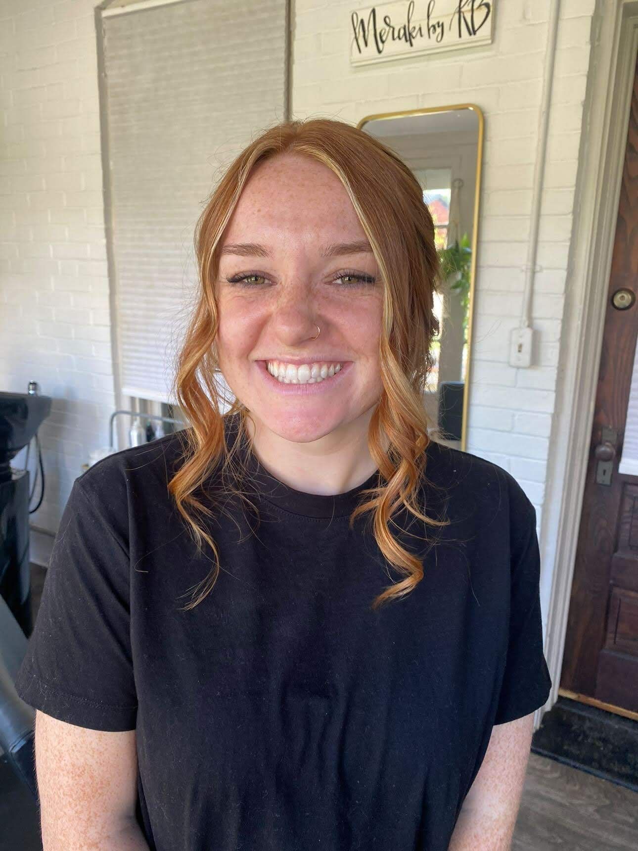 A woman with red hair is wearing a black shirt and smiling.