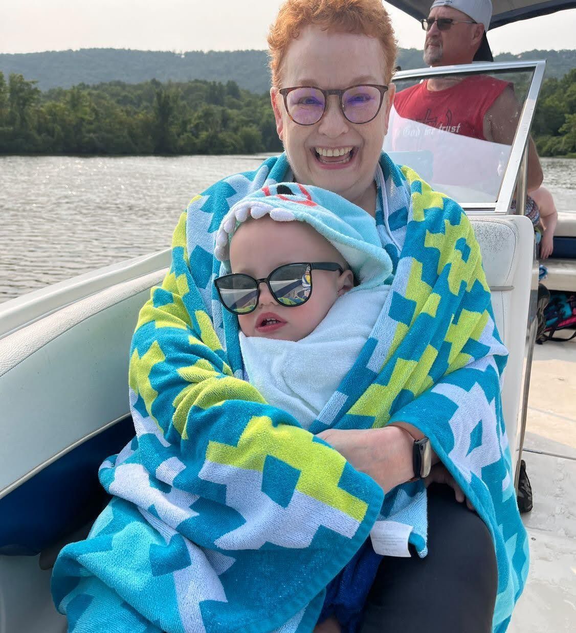 A woman is holding a baby wrapped in a towel on a boat.