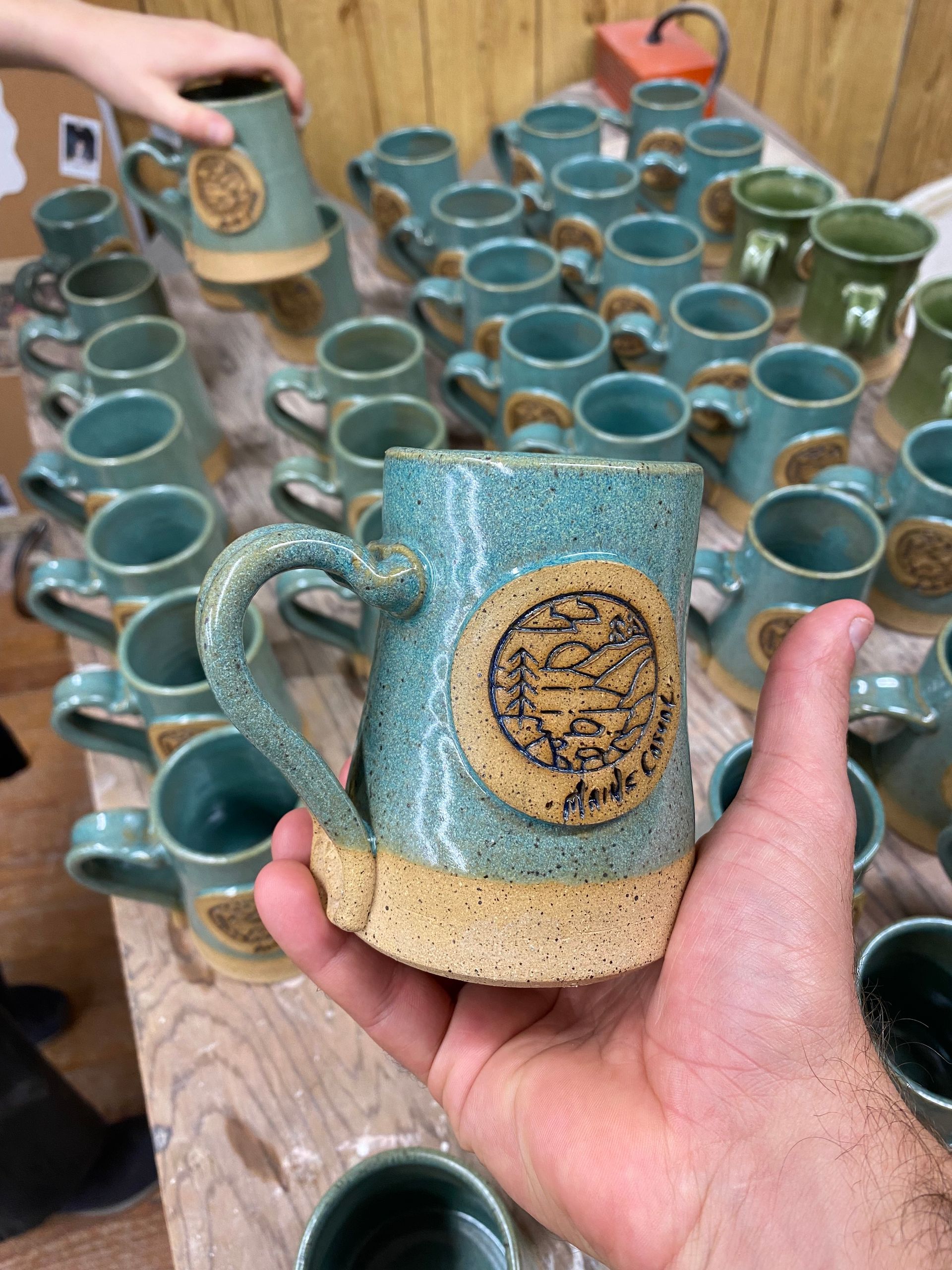 A person is holding a mug in front of a table full of mugs