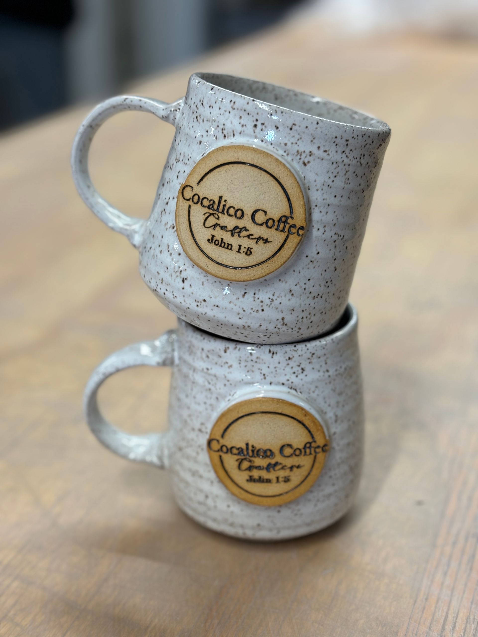 Two coffee mugs are stacked on top of each other on a wooden table.