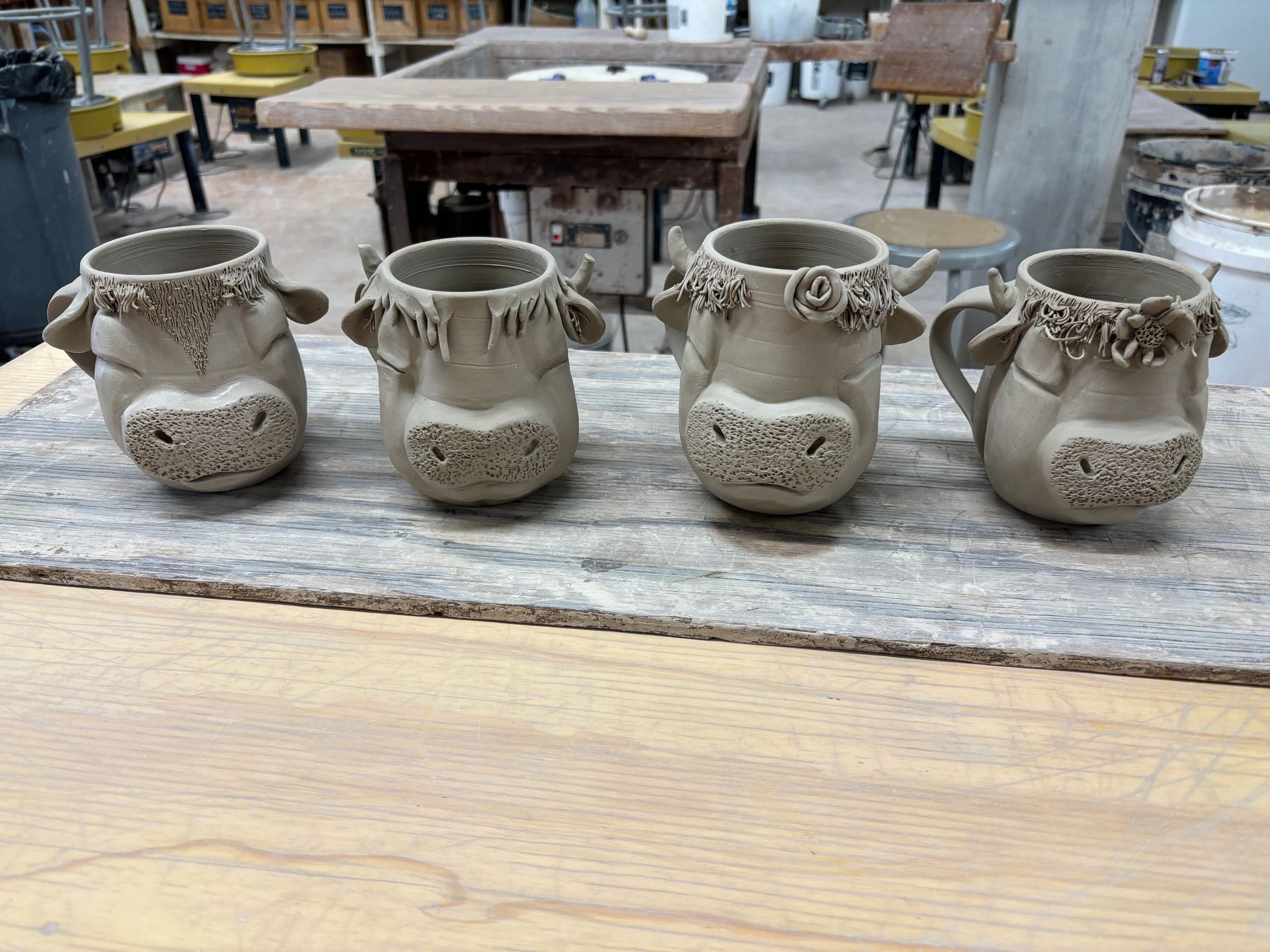 Four clay mugs with cow faces on them are sitting on a wooden table.
