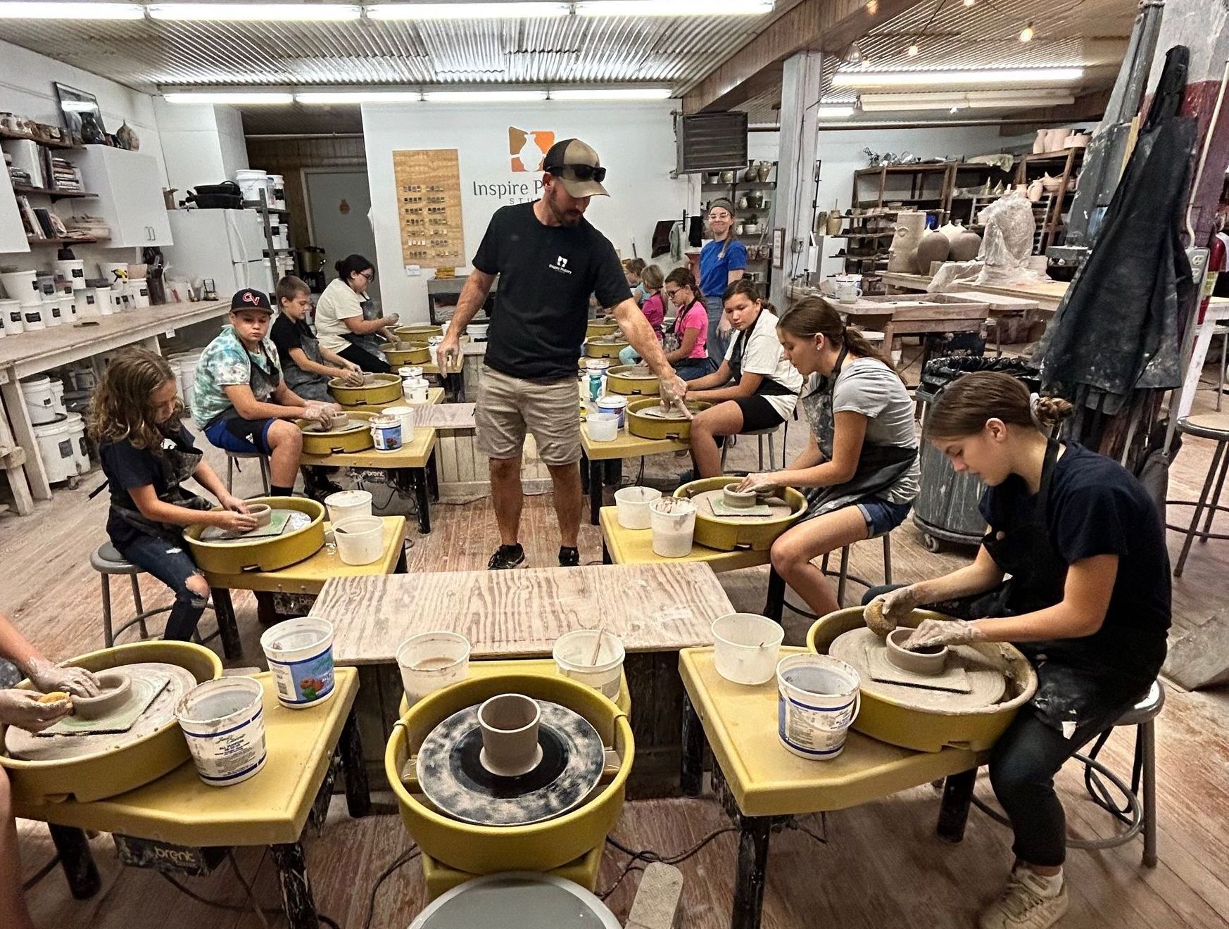 A group of children are sitting at tables in a pottery studio.