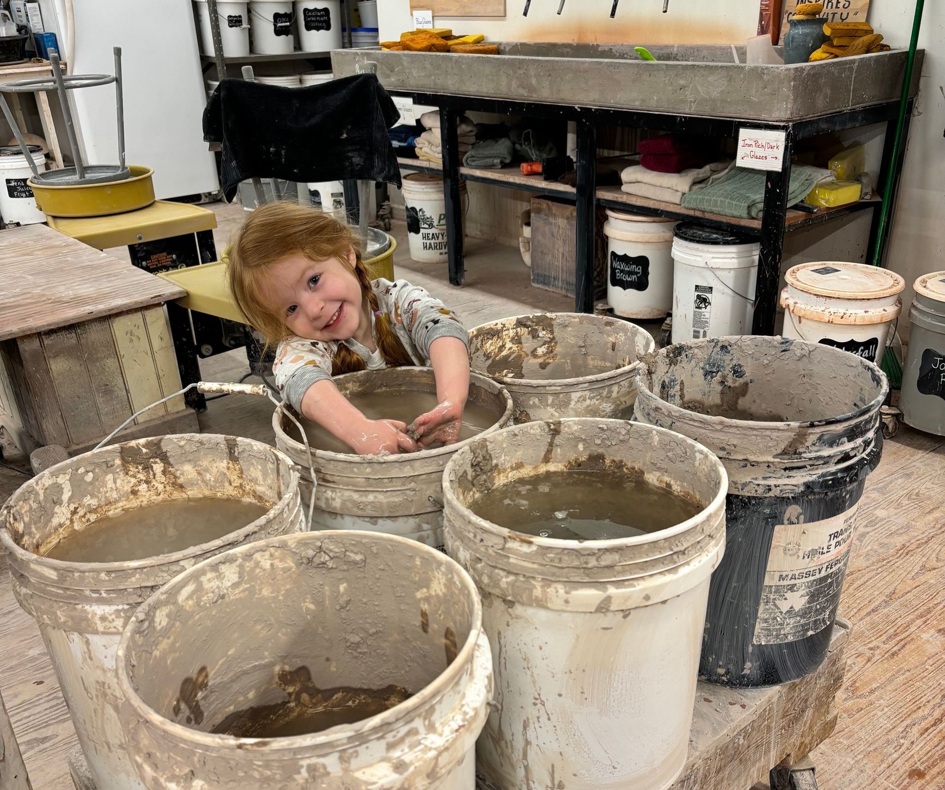 A little girl is sitting in a bucket of mud