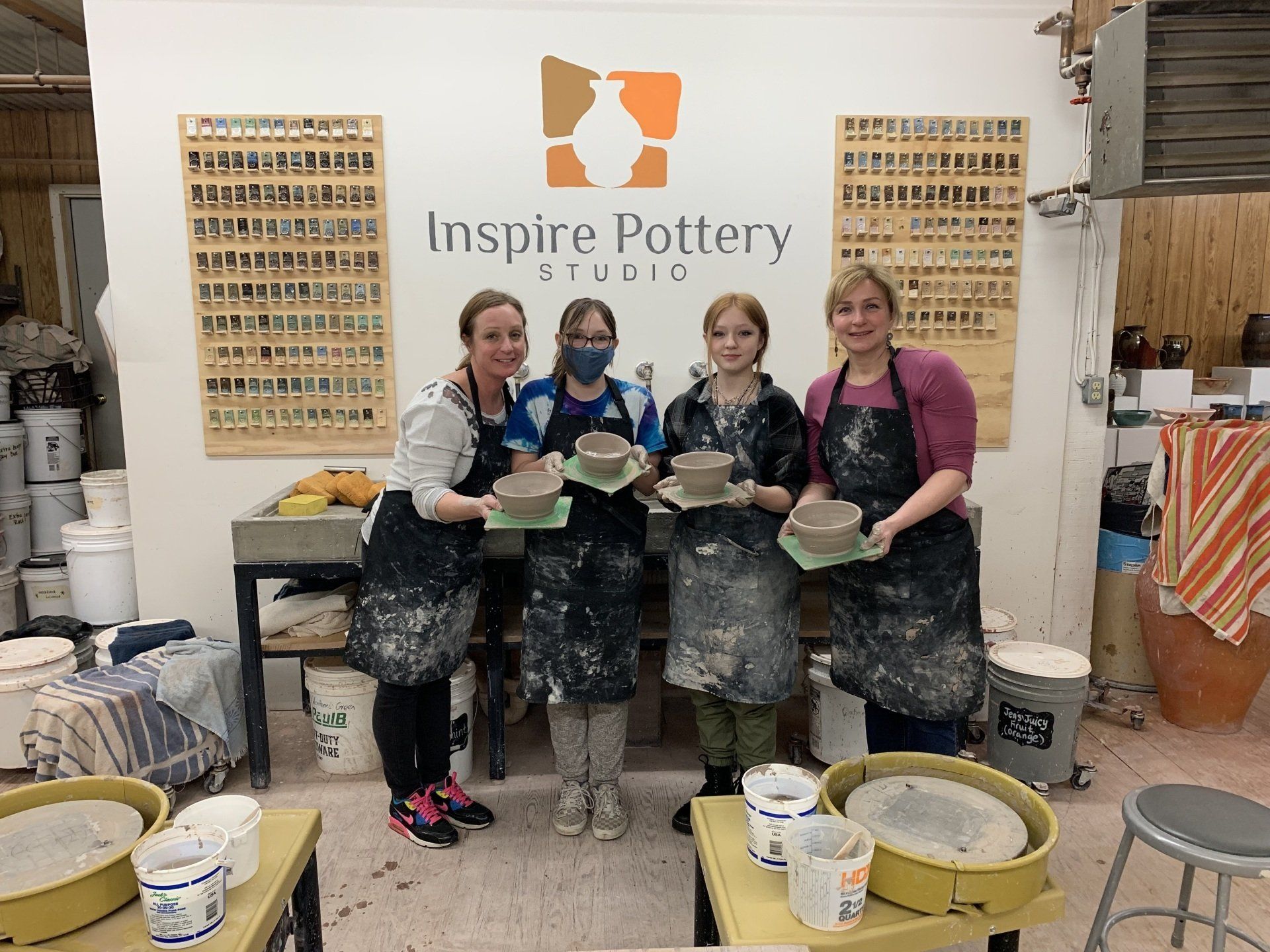 a group of women standing in front of a sign that says inspire pottery studio