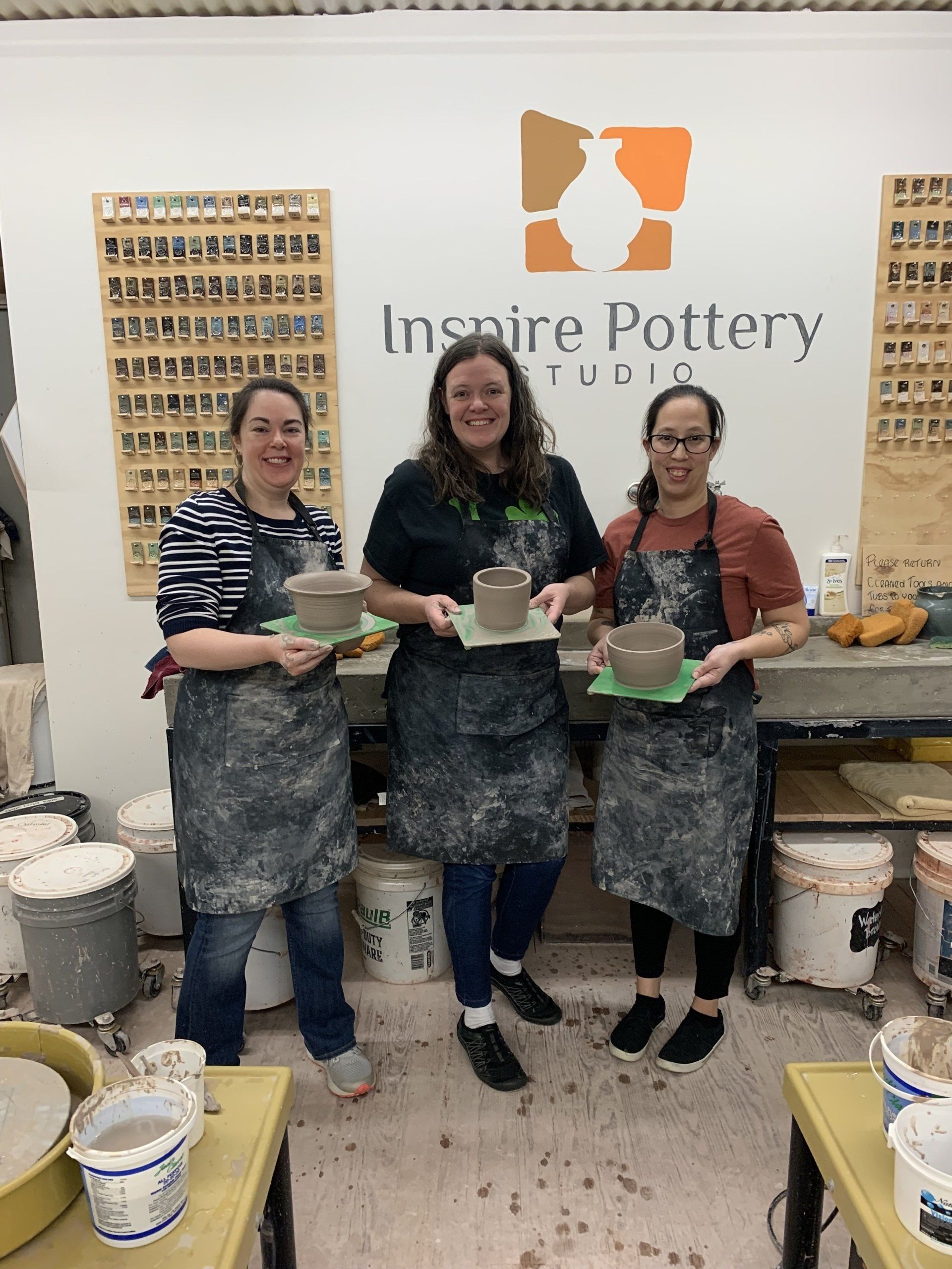 Three women are standing in front of a sign that says inspire pottery studio
