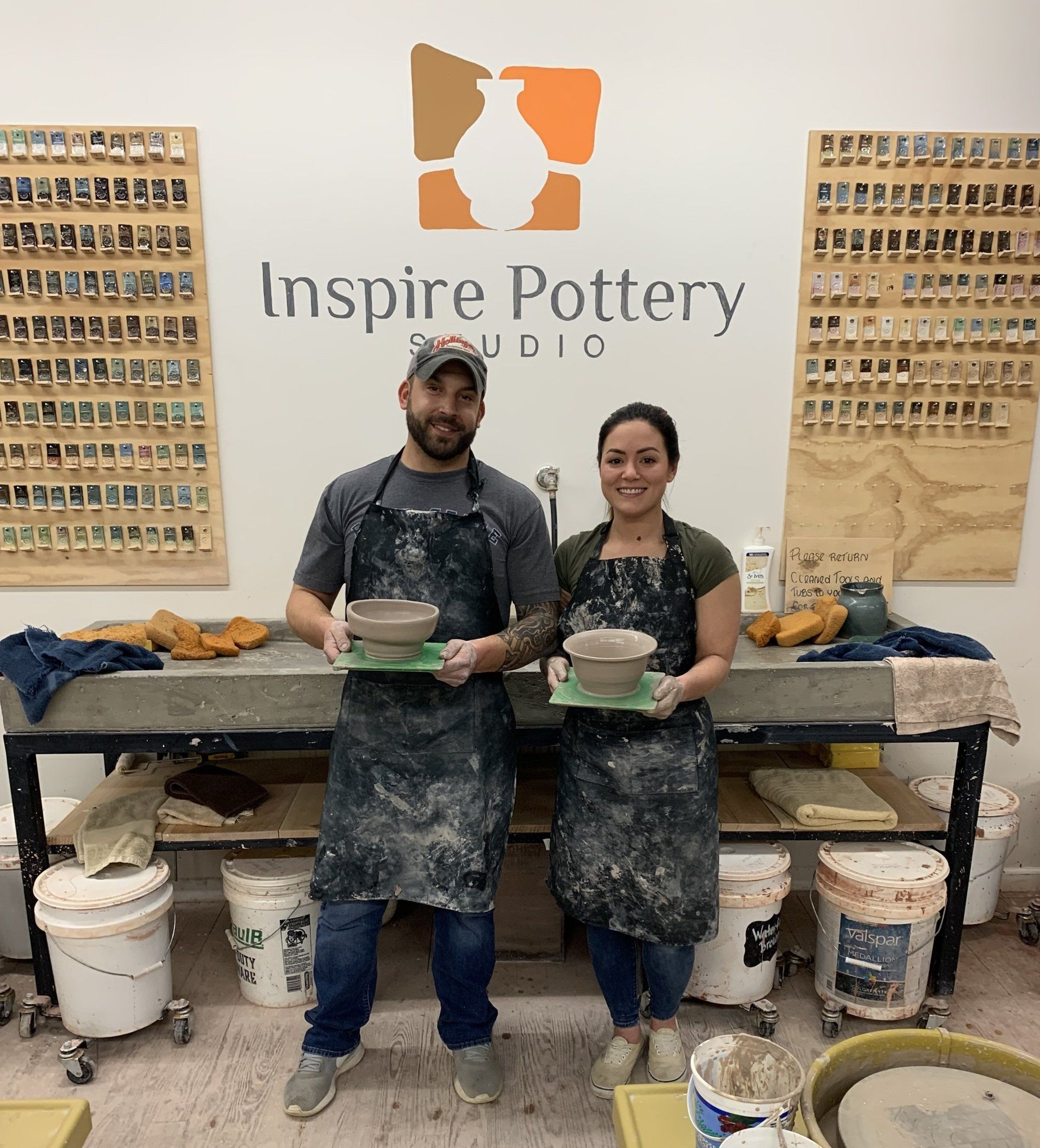 a man and a woman are standing in front of a sign that says inspire pottery