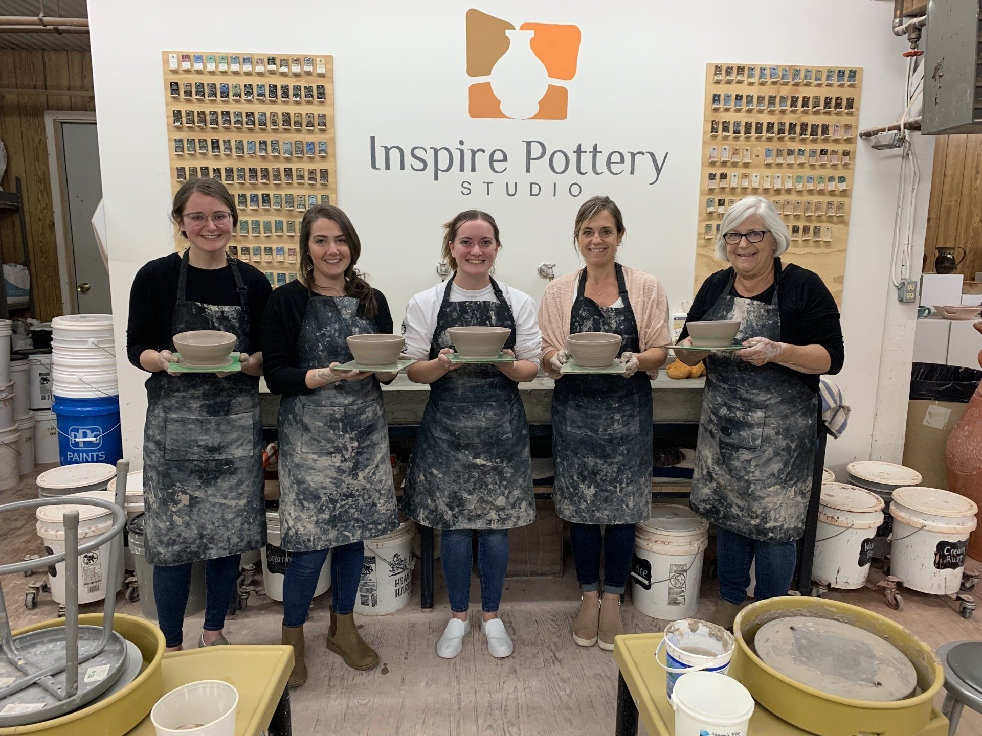 A group of women are standing next to each other in a pottery studio holding bowls.