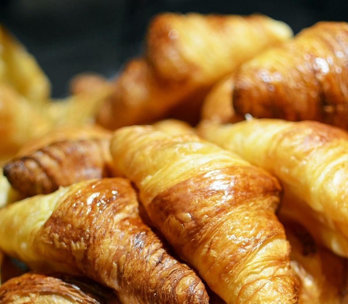 Golden, flaky croissants piled together, close-up.