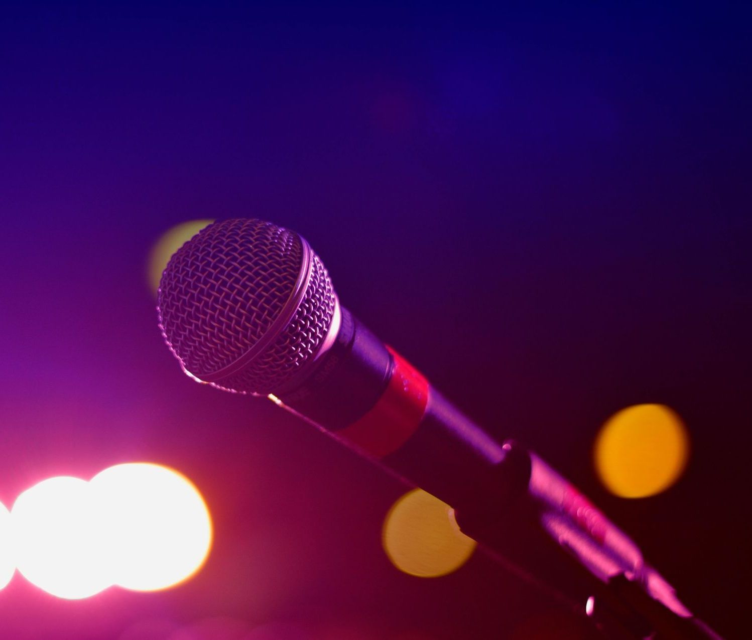 Microphone onstage with a blurred background of colorful lights, illuminated in purple and orange.