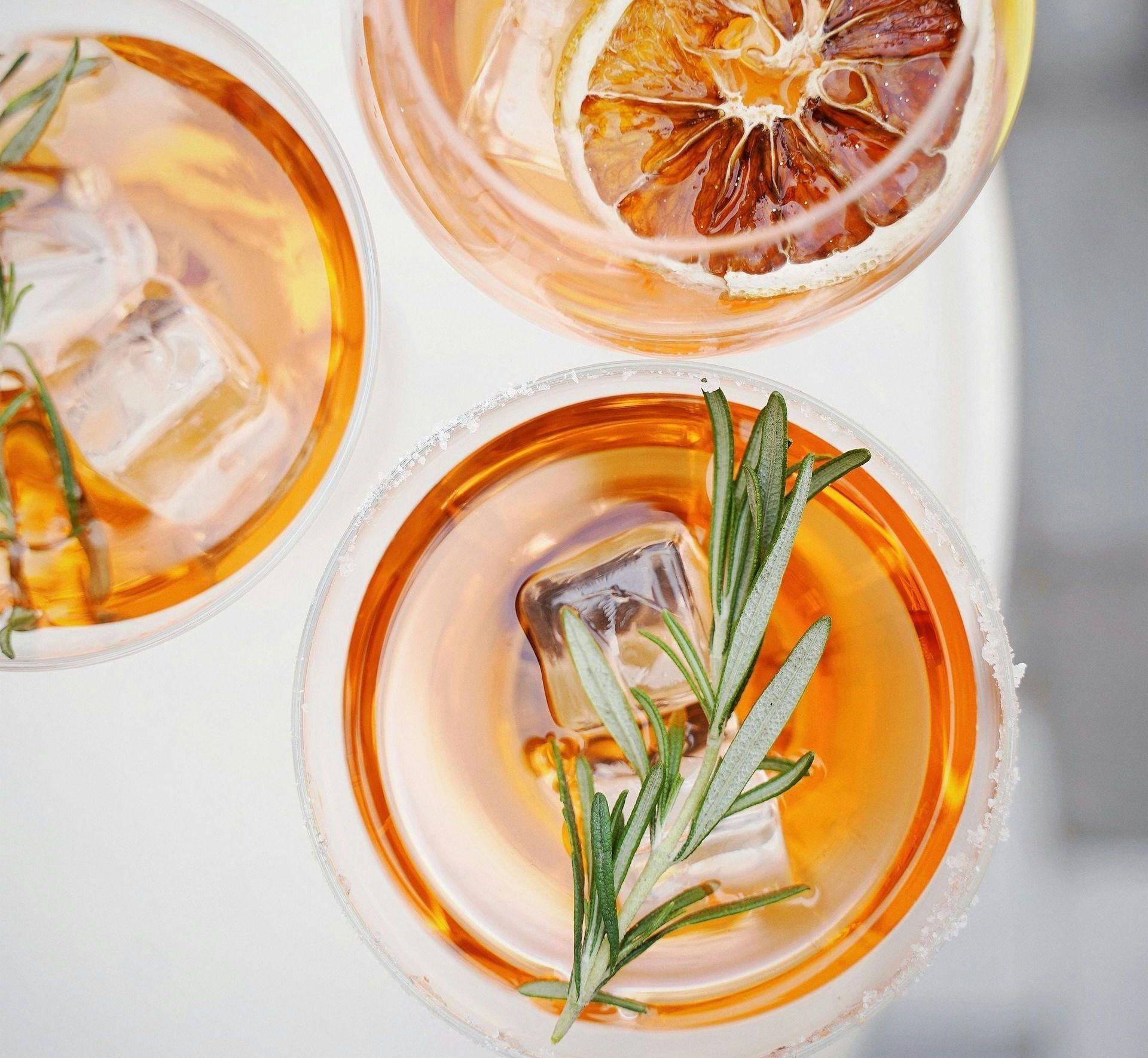 Three orange cocktails, garnished with rosemary and citrus, served in glasses with ice.