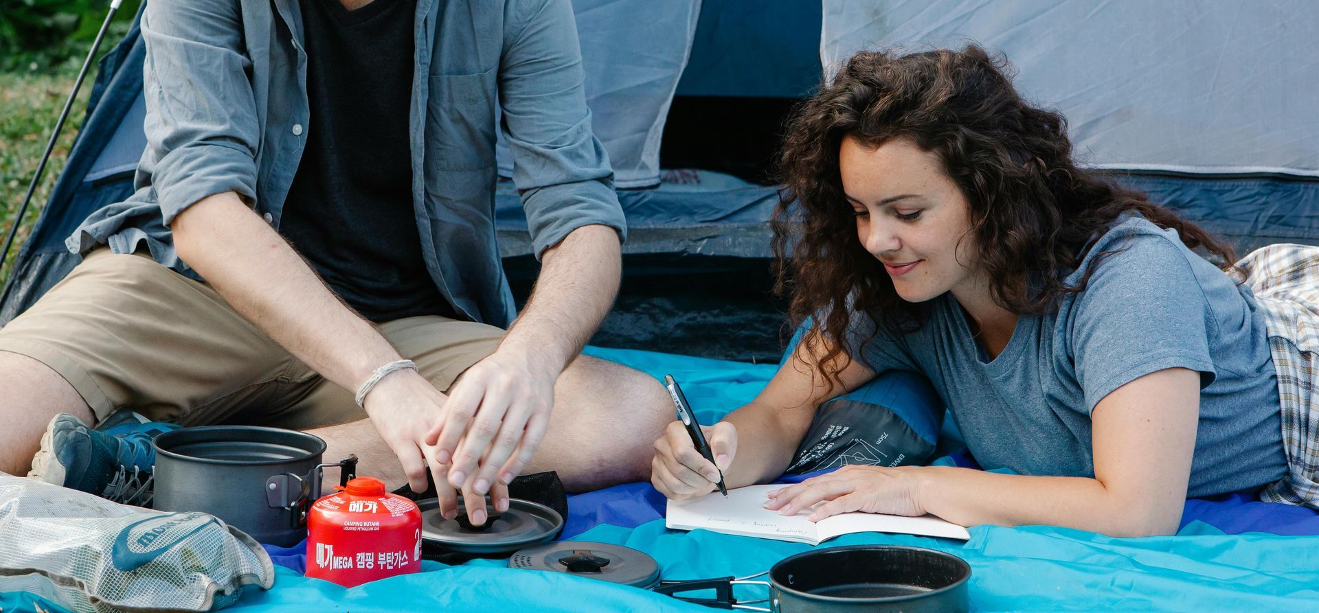 A man and a woman are sitting on a blue blanket in front of a tent.