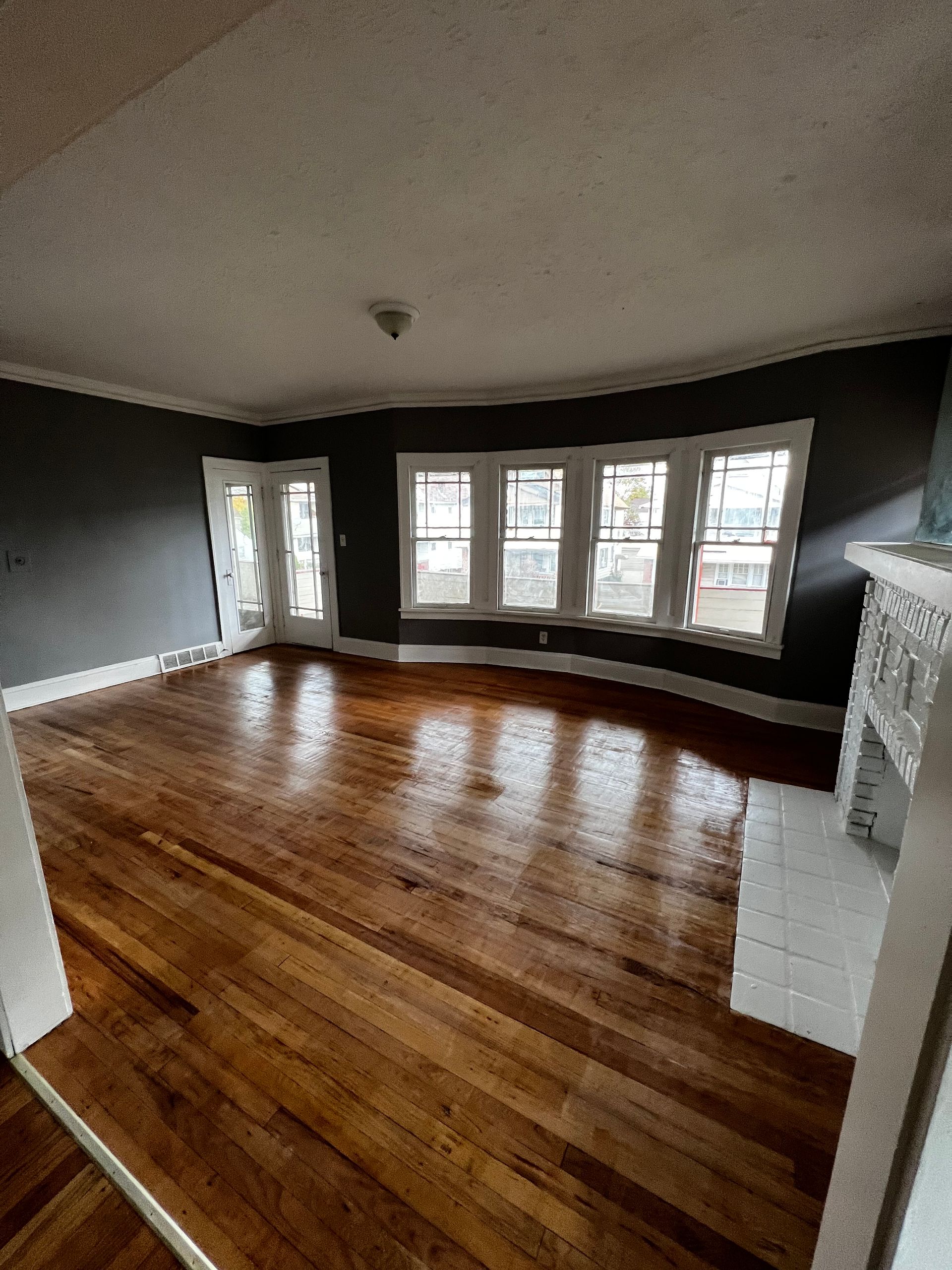 Empty living room with dark gray walls, hardwood floor, white trim, and a fireplace.