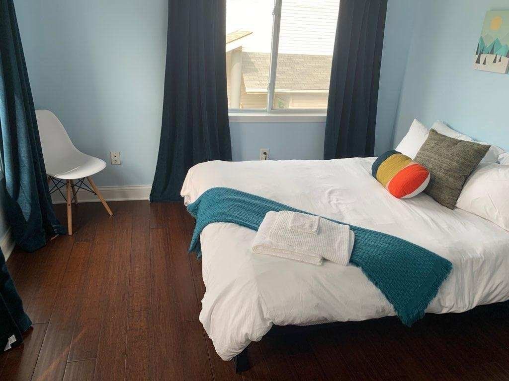 Bedroom with bed, chair, window, dark curtains, and wood flooring.