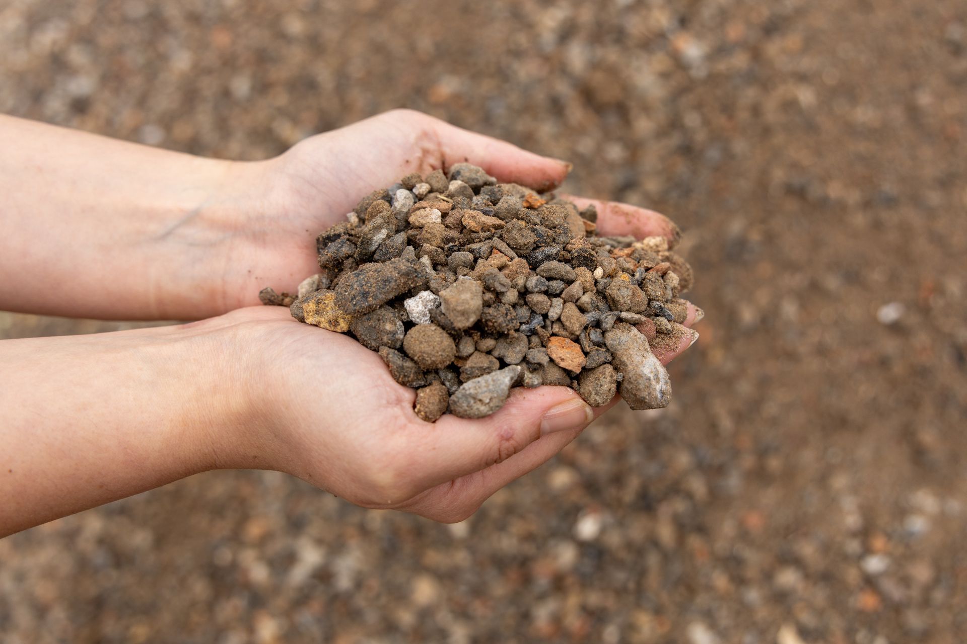 Hands Holding a Pile of Brown Gravel — Economy Waste Group | Skip Bins Central Coast In Mooney Mooney, NSW