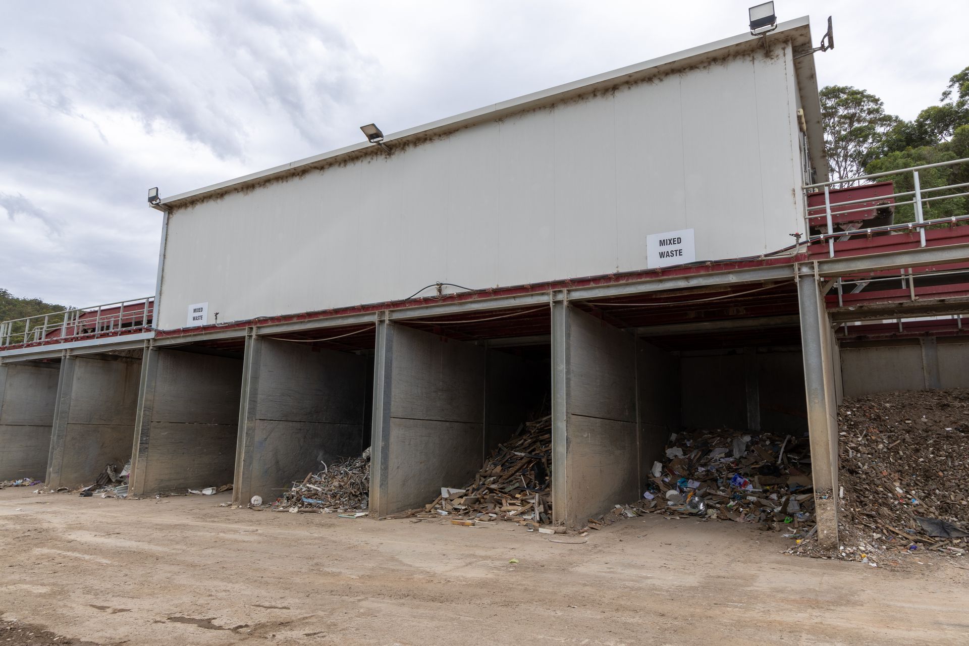 Waste sorting facility with concrete bins and overhead structure.— Economy Waste Group | Skip Bins 