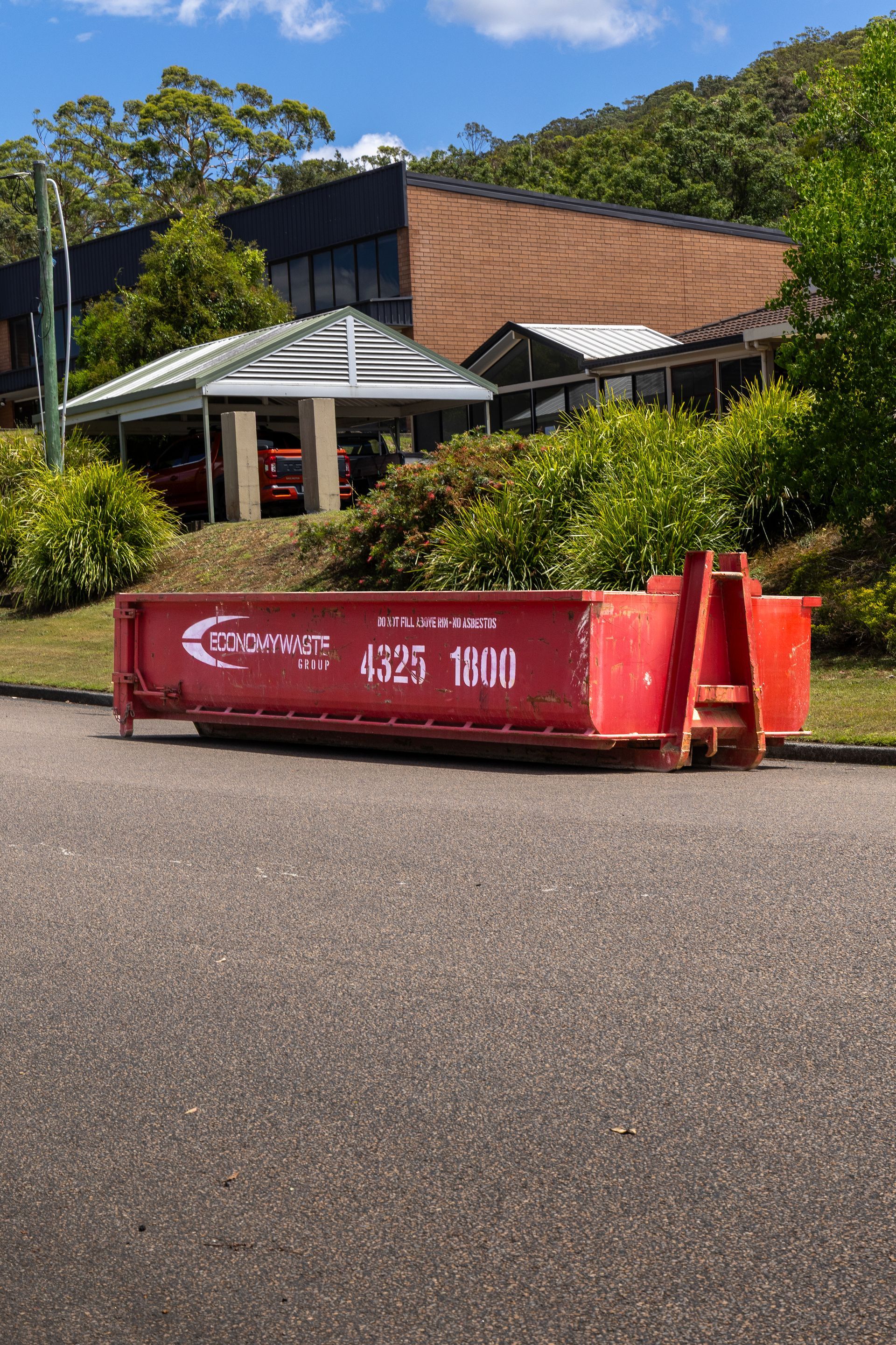 A Red Economy Waste Dumpster on a Green Lawn — Economy Waste Group | Skip Bins Central Coast In West Gosford, NSW