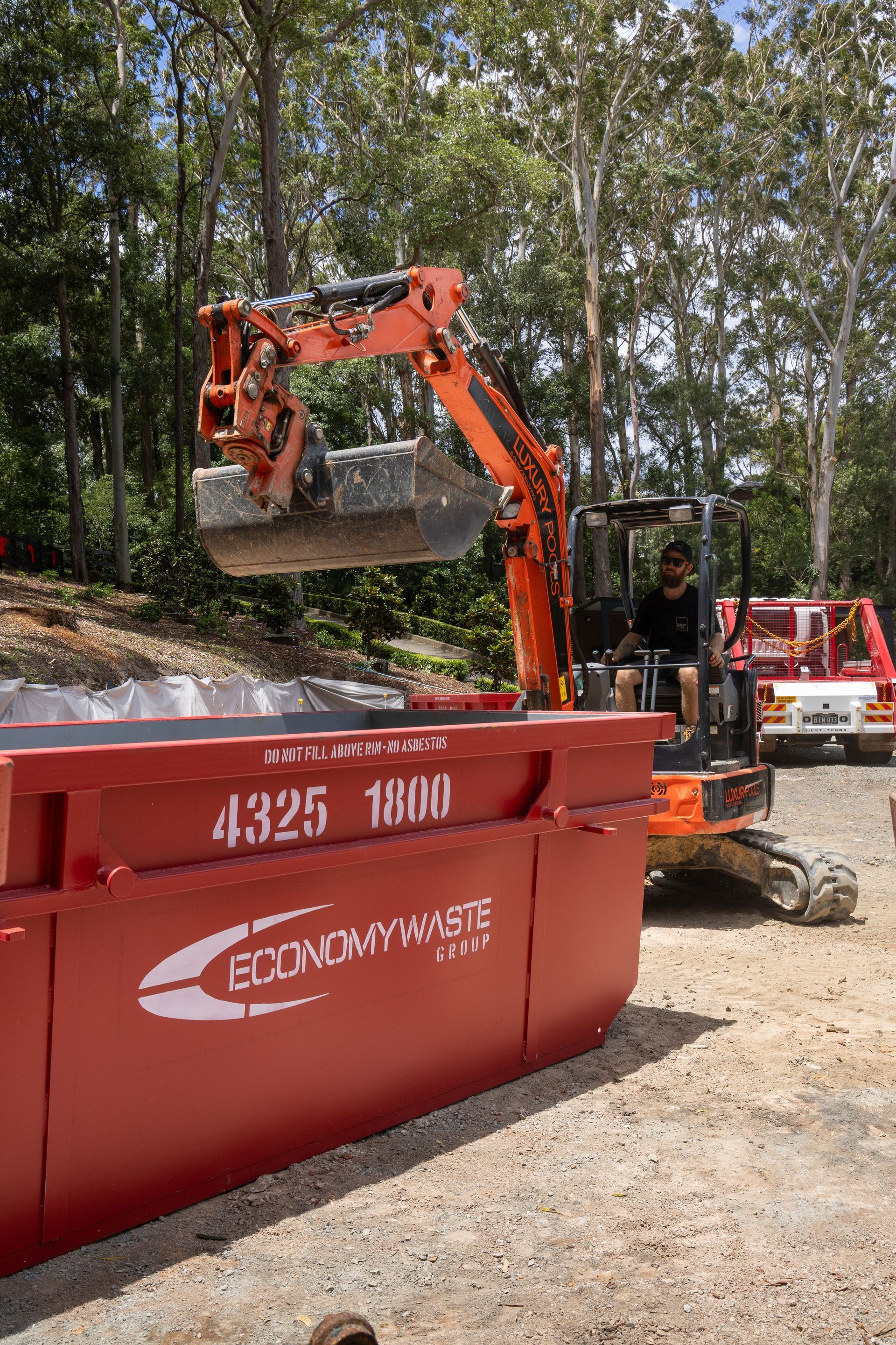 A Man And Woman Standing In Front Of A Red Dumpster — Economy Waste Group | Skip Bins Central Coast In West Gosford, NSW