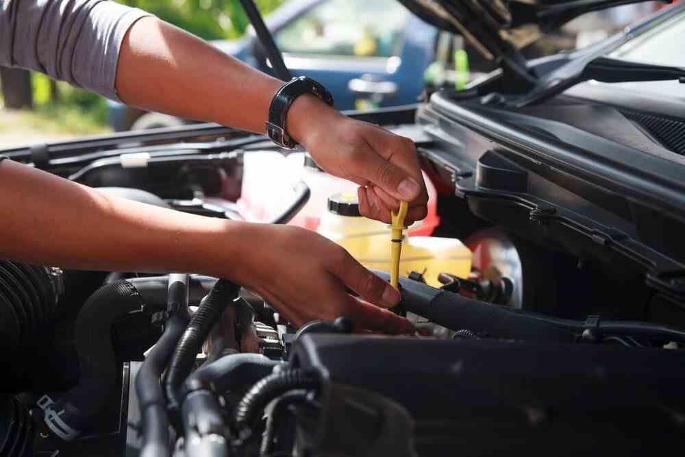 A Man is Checking the Oil Level of a Car With a Dipstick — Innisfail Pro Motors In Tablelands, QLD