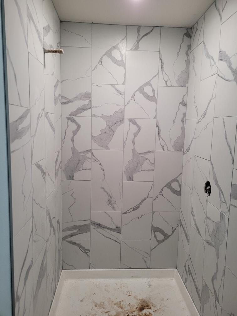 Tiled shower with marble-like pattern on walls, shower head, and small mud-like material on the floor.