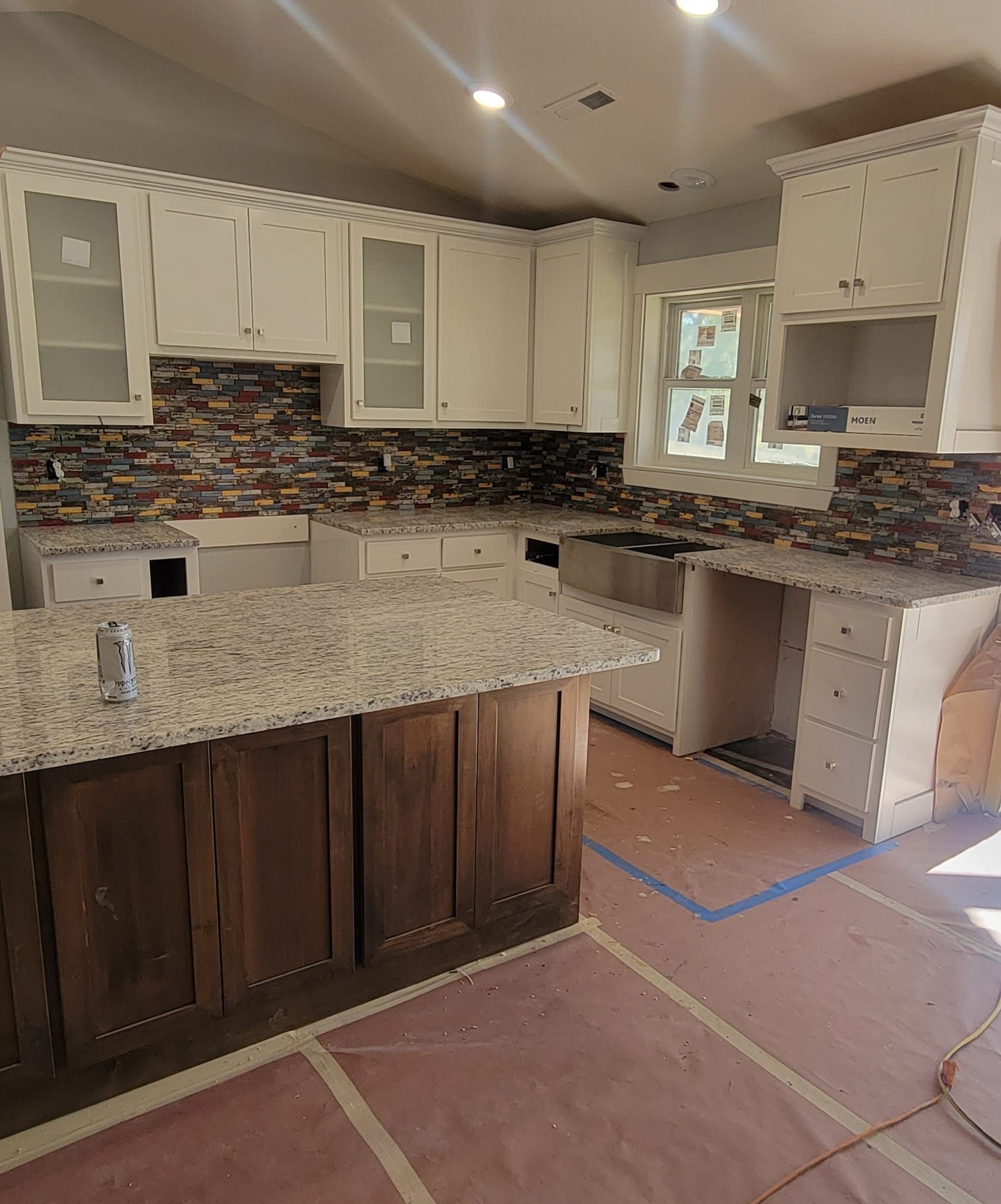 Kitchen with white cabinets, stone countertop, brown island, and multi-colored backsplash.