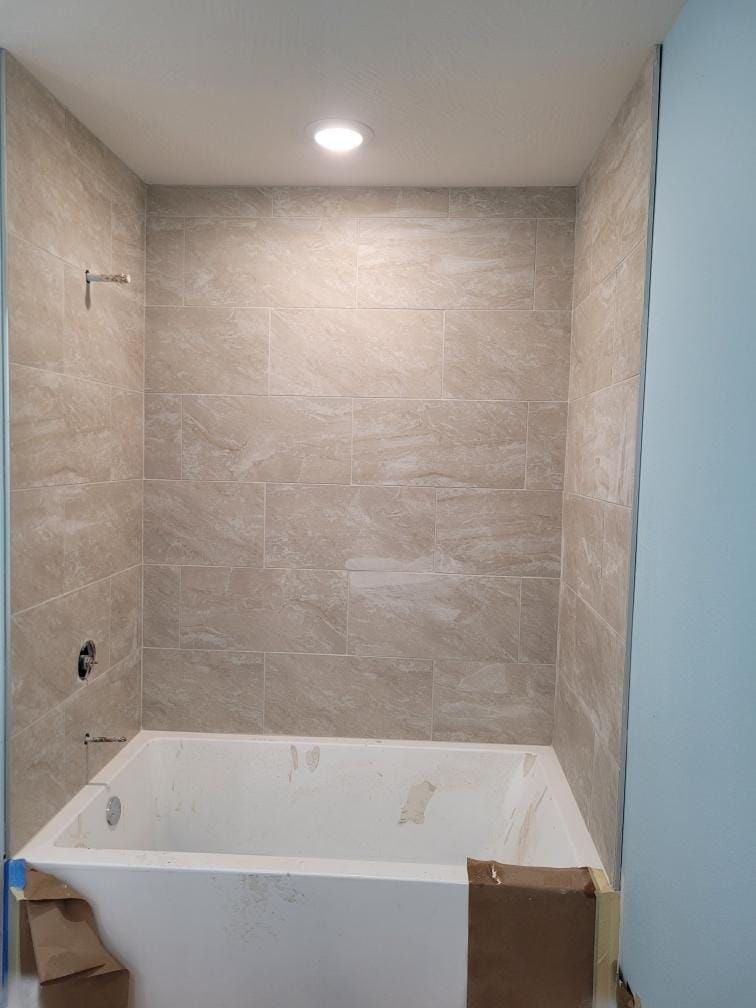 Bathroom alcove with tiled walls, white bathtub, and light fixture. Blue wall on the right.