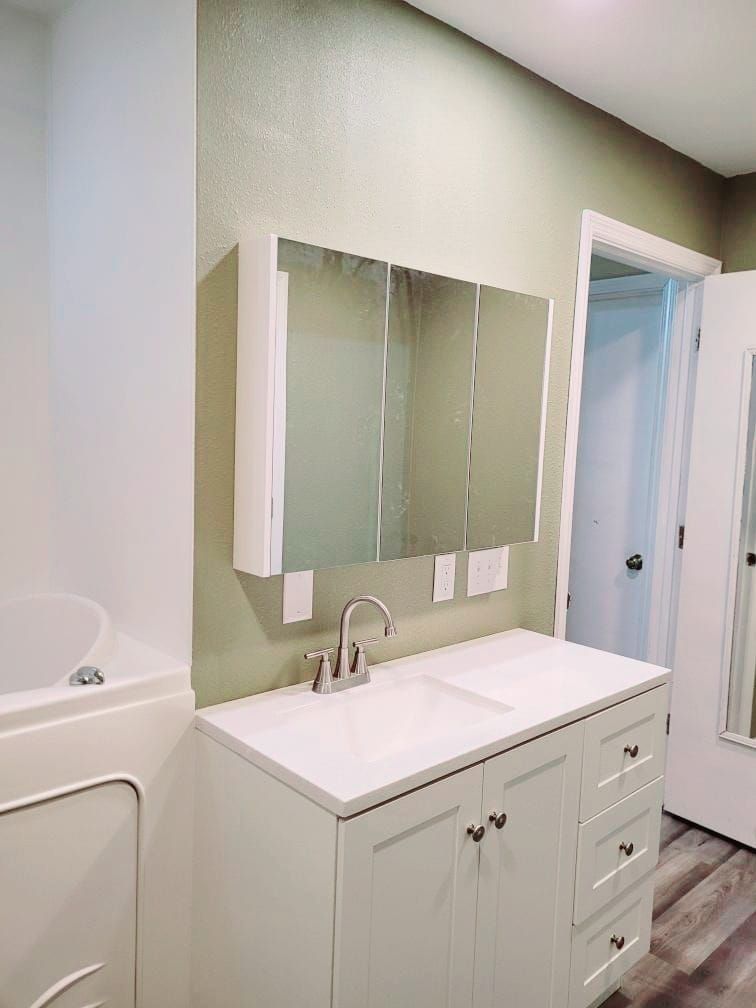 White bathroom vanity with sink and mirror, light green walls, and open door.