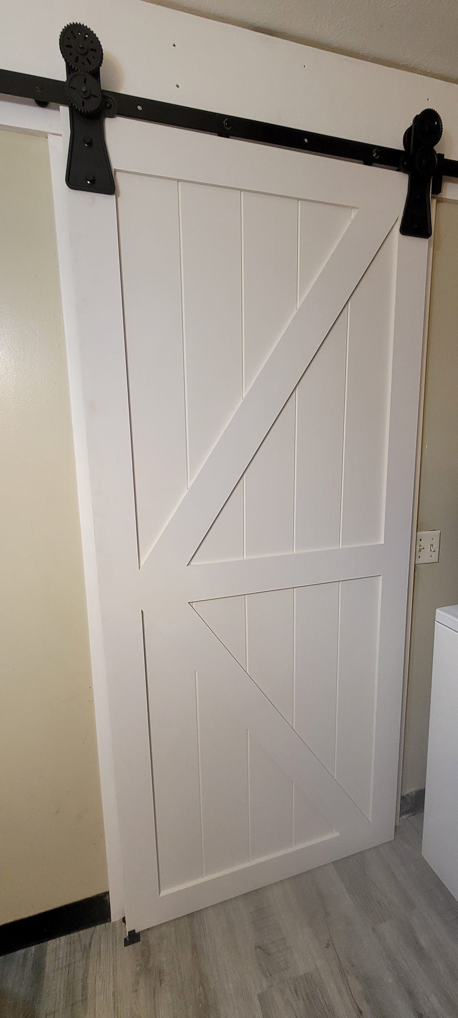 White barn door with black hardware, mounted on a wall with cream-colored paint and gray floor.