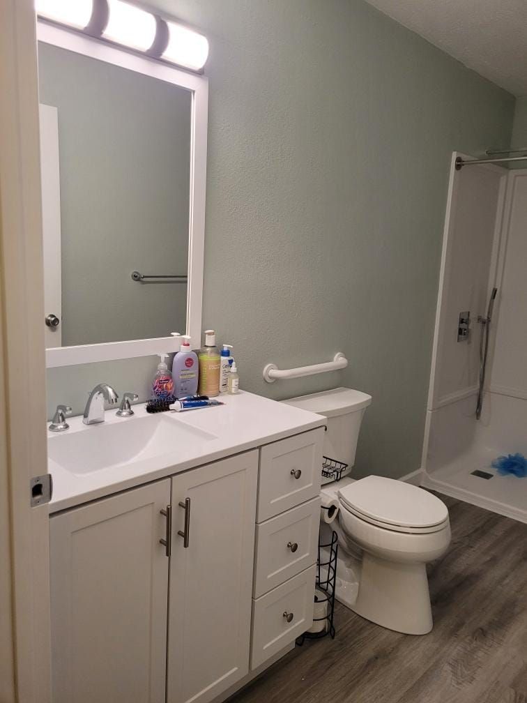 Bathroom with white vanity, toilet, and shower against light green walls.