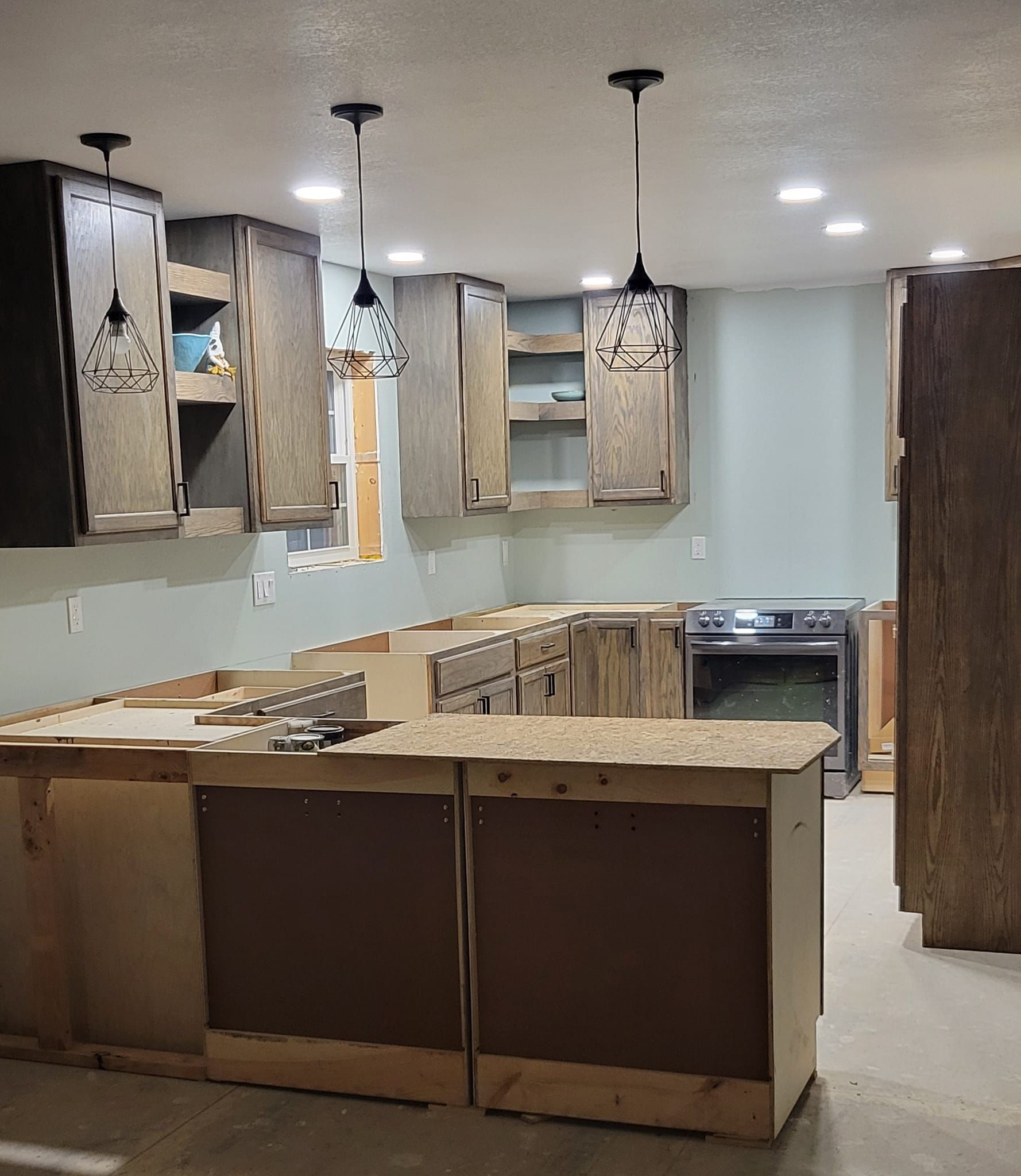 Kitchen under construction with upper cabinets, island, stove, and pendant lights.