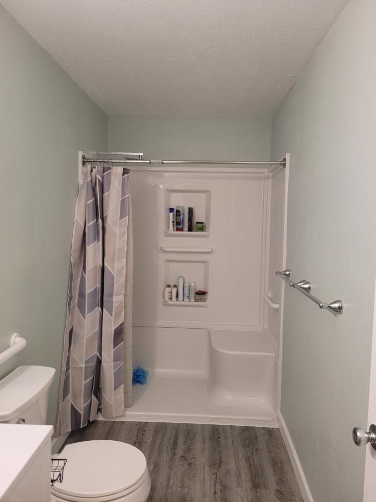 Bathroom with white shower and fixtures, gray patterned shower curtain, and light green walls.