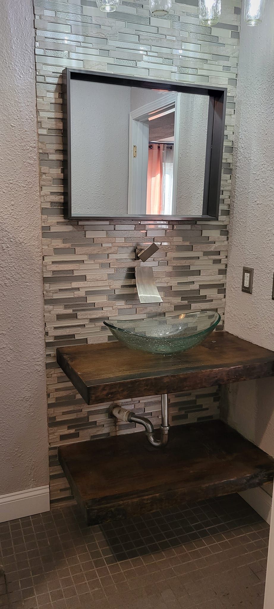 Bathroom with a glass bowl sink on wooden shelves, a mirror, and tiled walls.