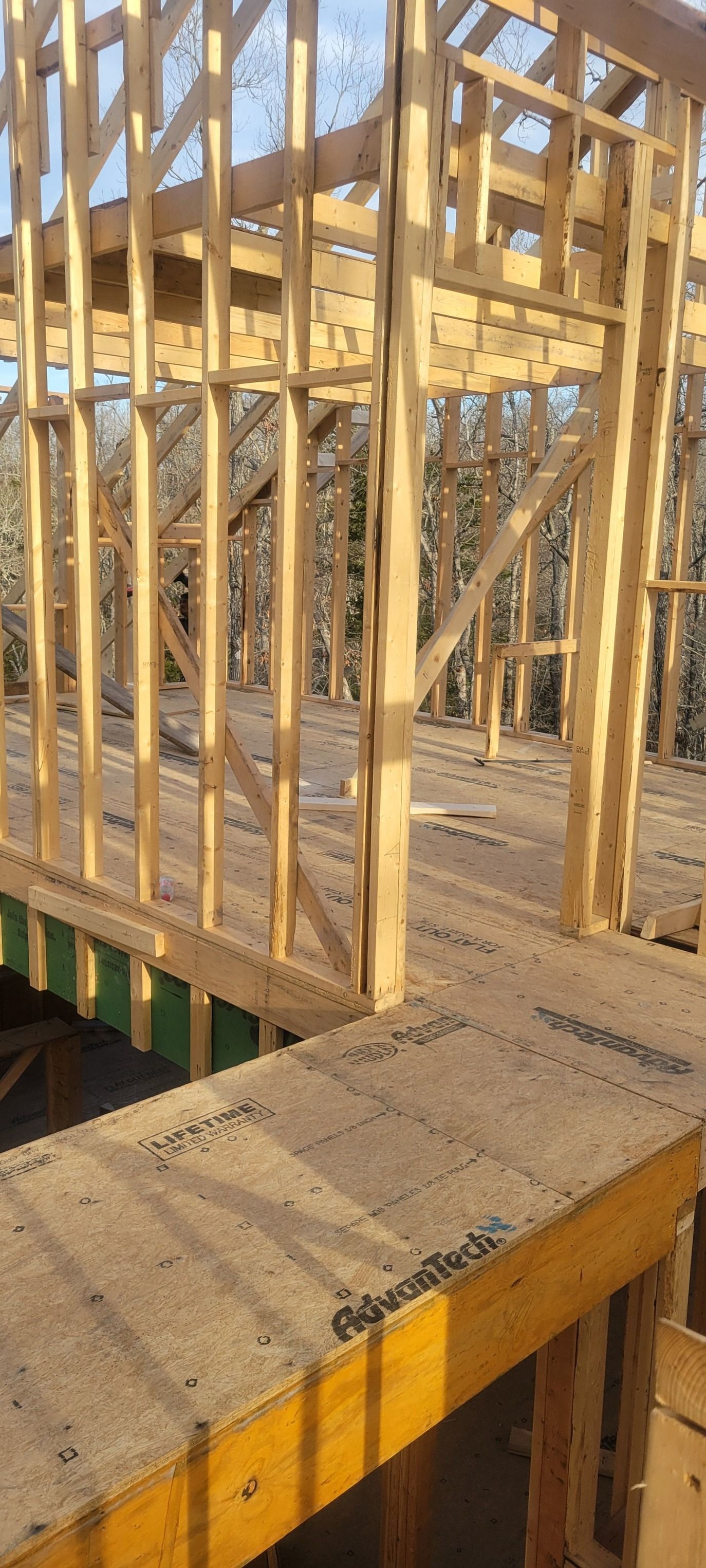 Wooden house frame under construction. Interior view with wood beams and flooring, surrounded by trees.