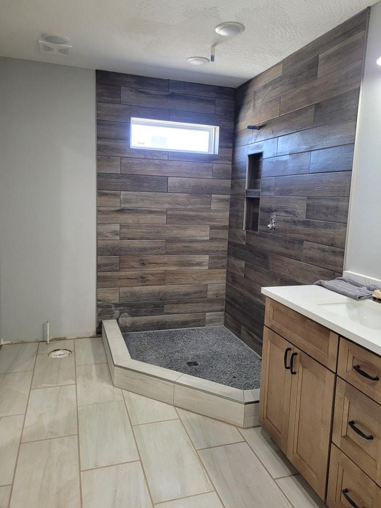 Newly renovated bathroom with wood-look tile shower, gray walls, and light wood vanity.
