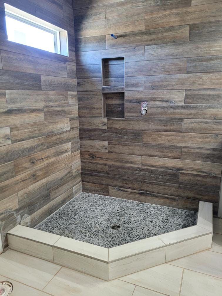 Shower with wood-look tile walls, gray pebble floor, built-in shelf, and light tile trim.