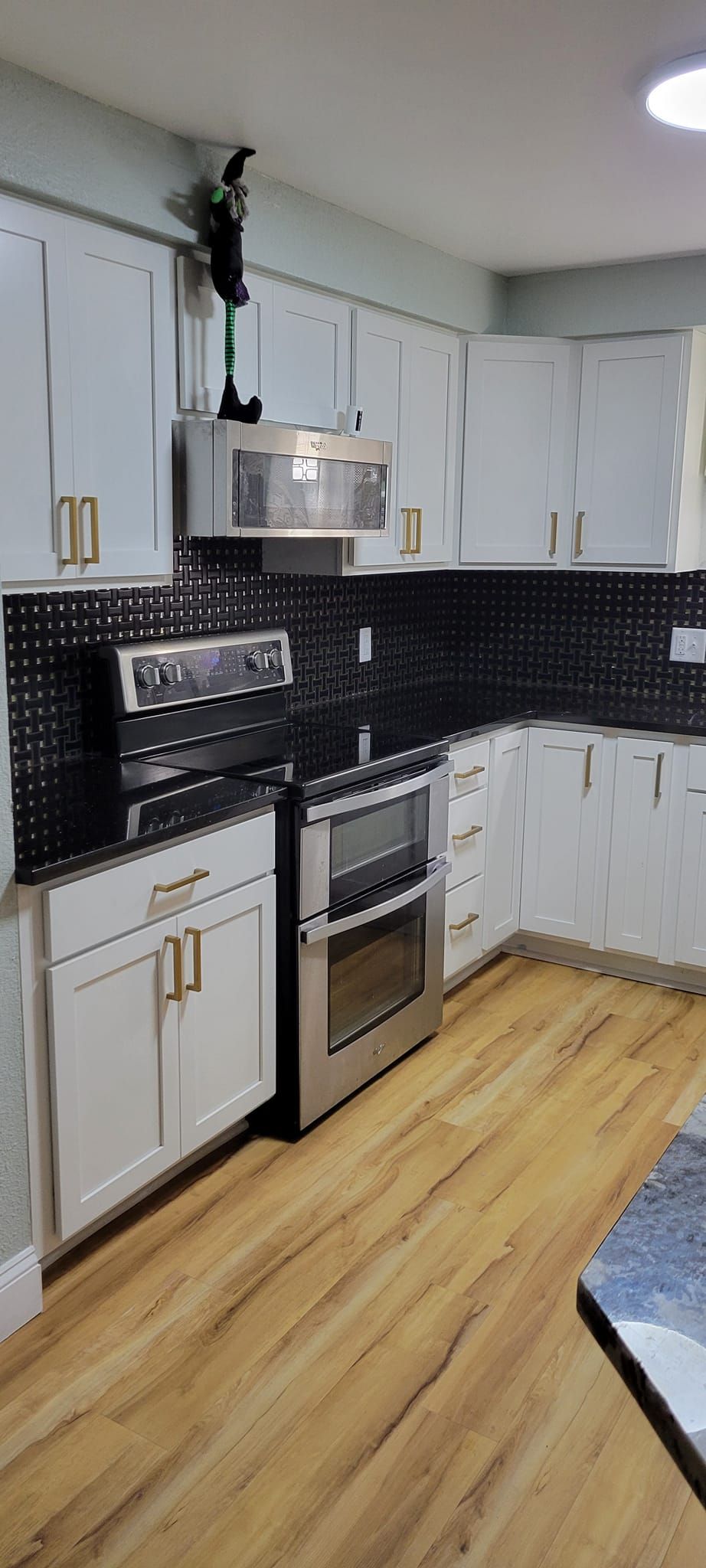 Kitchen with white cabinets, black backsplash, stainless steel appliances, and wood-look flooring.