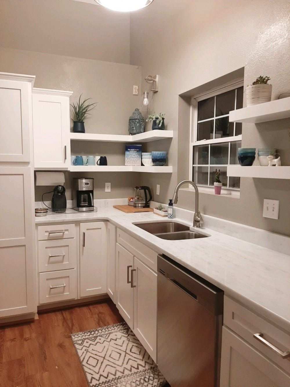 White kitchen with cabinets, floating shelves with decor, stainless steel appliances, and wood floor.