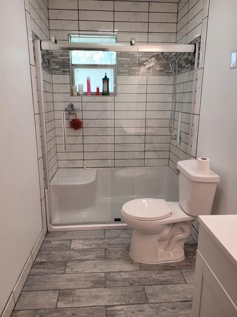 Bathroom with shower, toilet, and gray tiled floor and white walls.