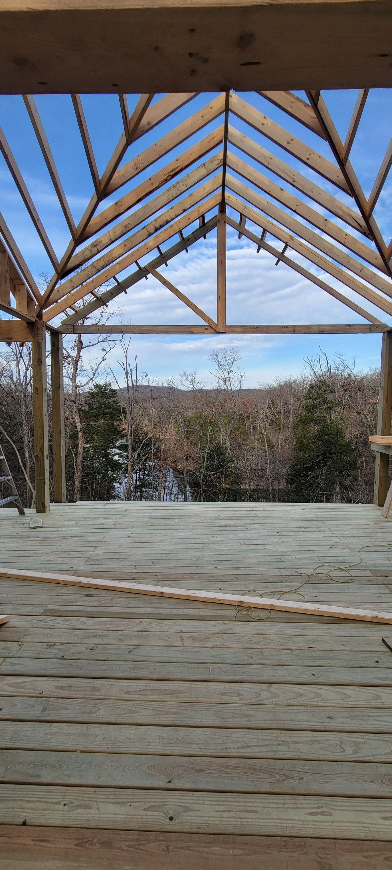 Wooden structure under construction, framing a view of trees and sky.