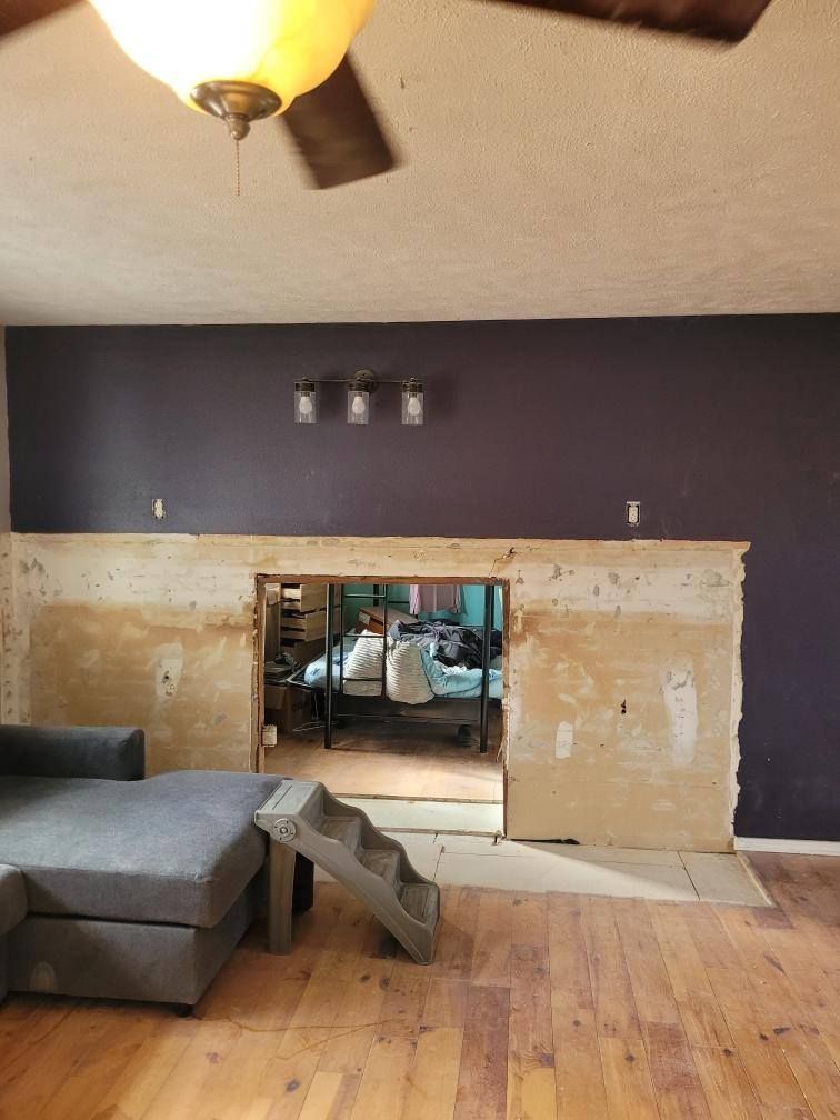 Living room renovation with a purple accent wall, exposed fireplace, and gray sectional.