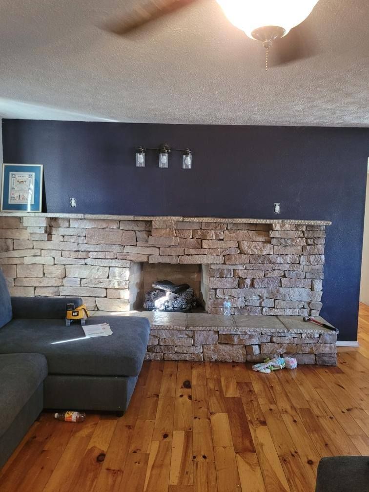 Stone fireplace against a dark blue wall in a living room with wooden floors.