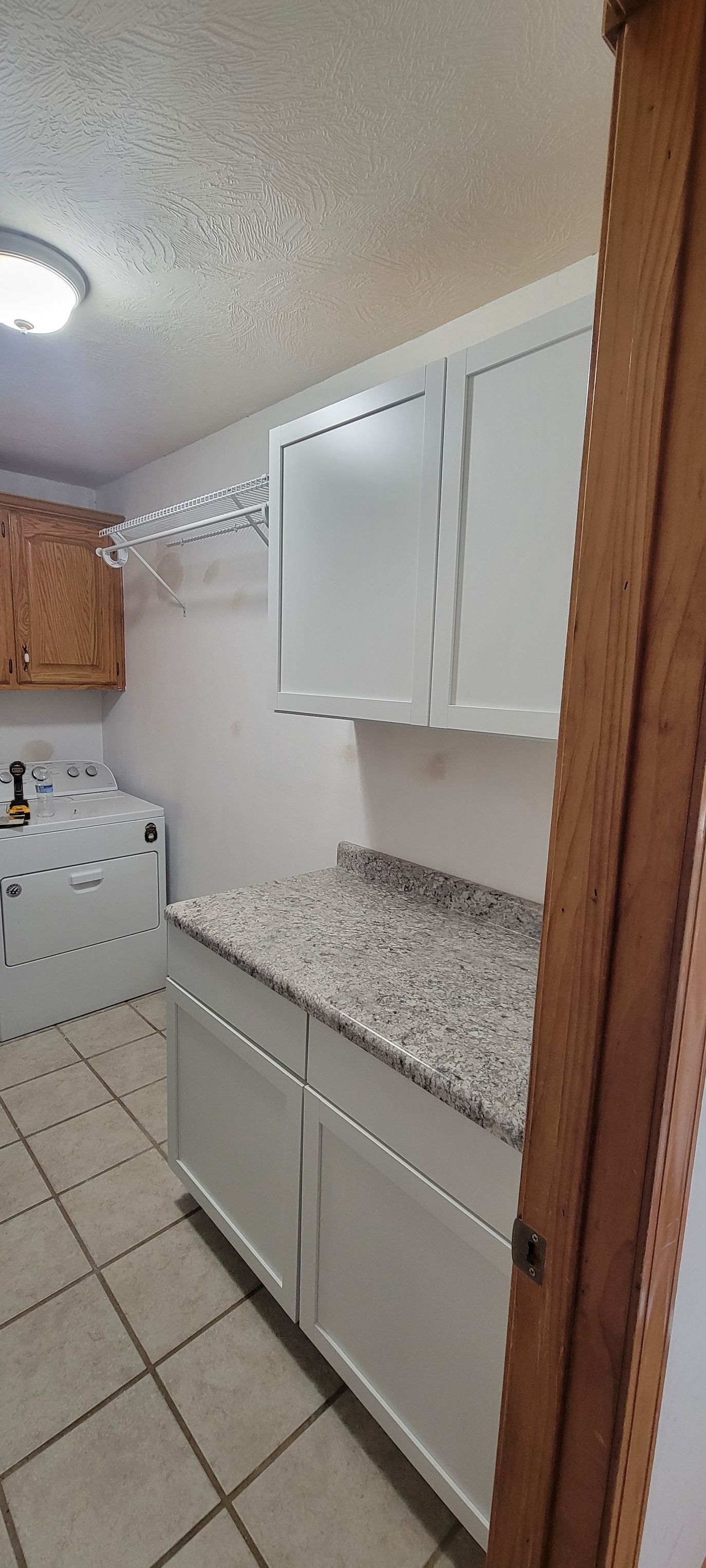 Laundry room with white cabinets, speckled countertop, and tiled floor. A washing machine is visible.
