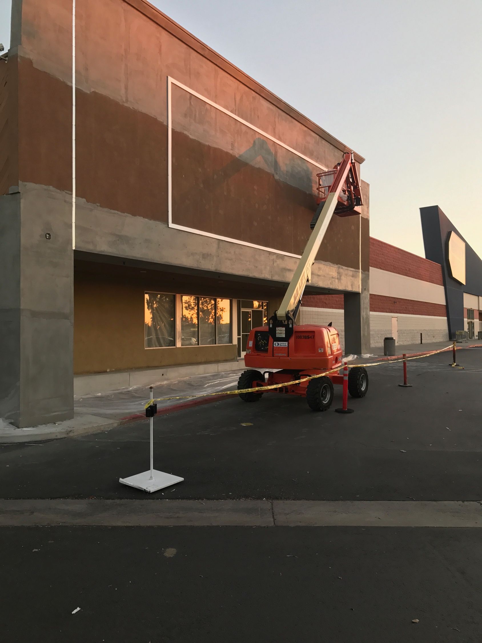 Construction of building exterior with lift, caution tape, and brown stucco.